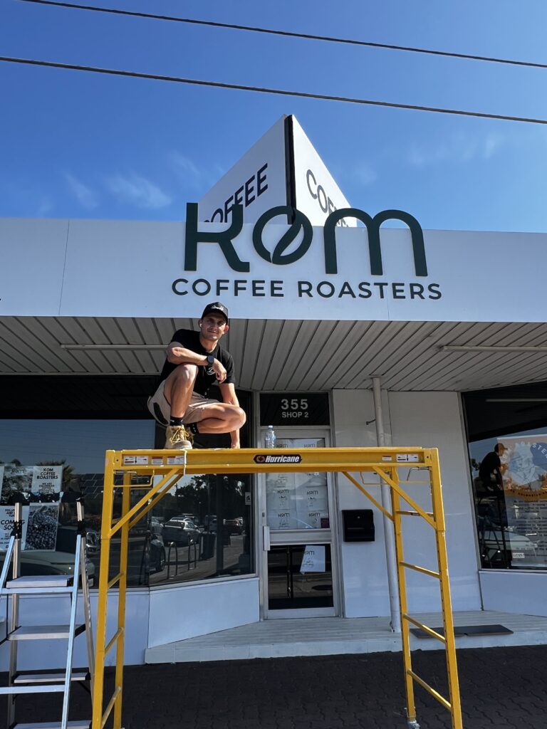 Diegodalo installing the KOM Coffee Roasters facade sign from a scaffold