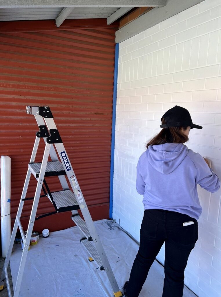 Carolina drawing the Burton TV mural design onto the primed brick wall