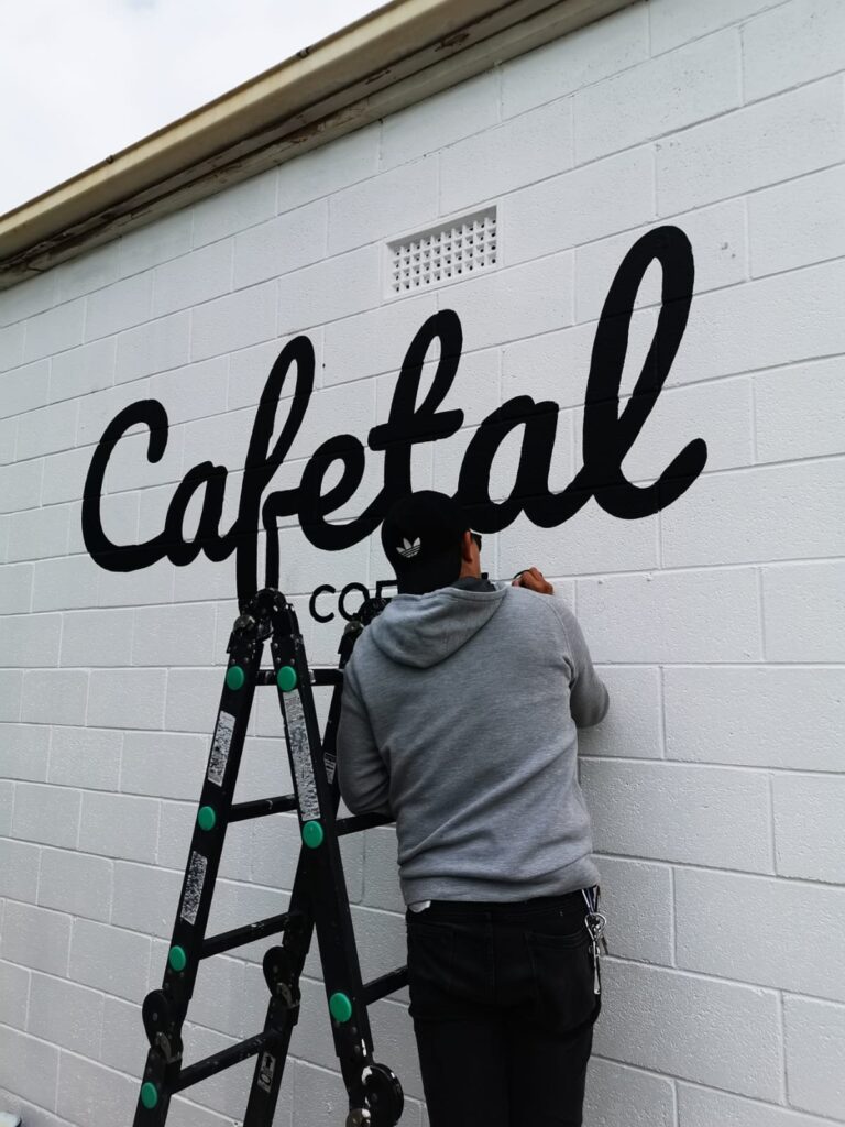 Diegodalo hand-painting the Cafetal Coffeeco logo on a brick wall in Kent Town