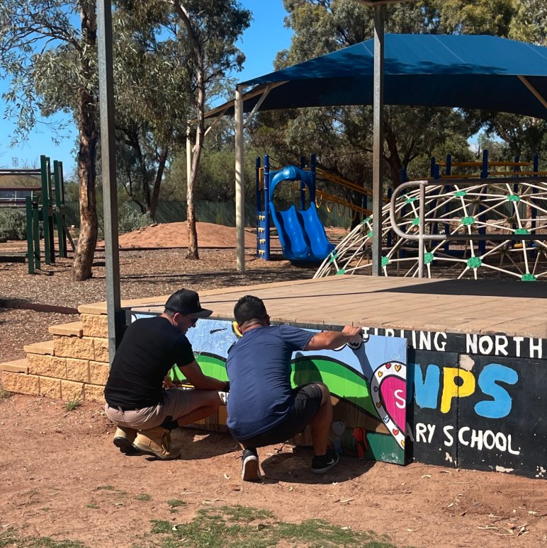 Two painters fixing hand-painted mural panels to the school stage at Stirling North