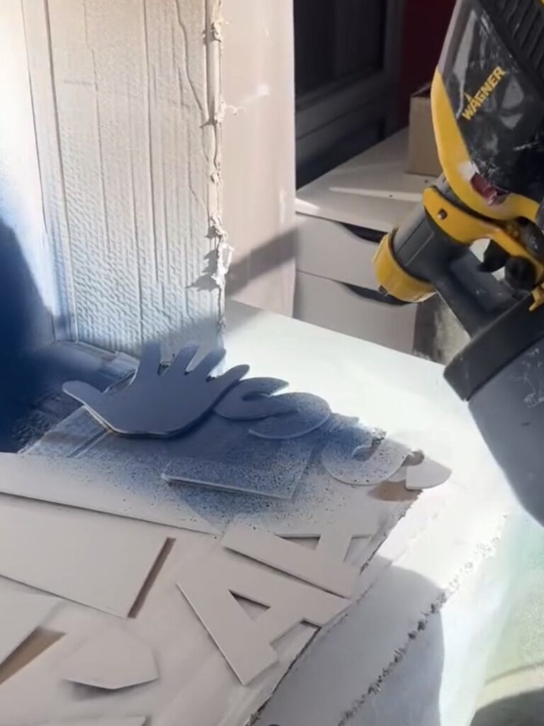 Spray-painting the laser-cut MDF LASSA logo and letters with a paint spray gun