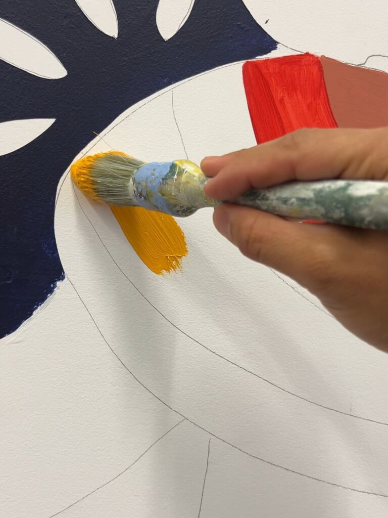 Hand-painting the LASSA mural with a brush, filling colour inside the pencil outlines