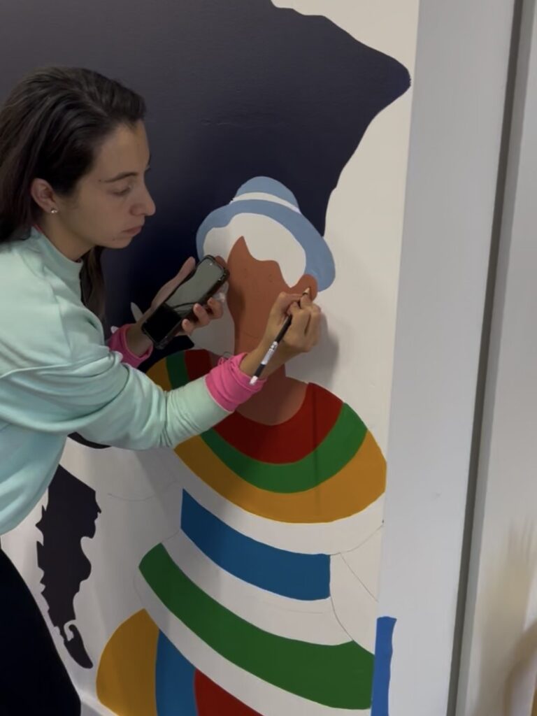 Carolina hand-painting the fine details of the figure on the LASSA mural in Adelaide