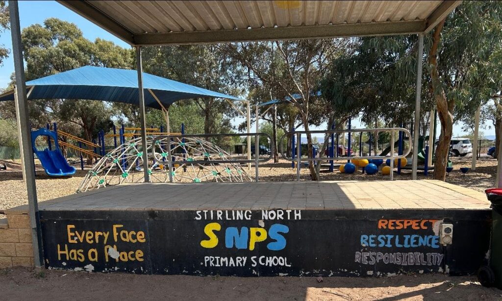 School stage before the mural, with faded hand-painted school name and values