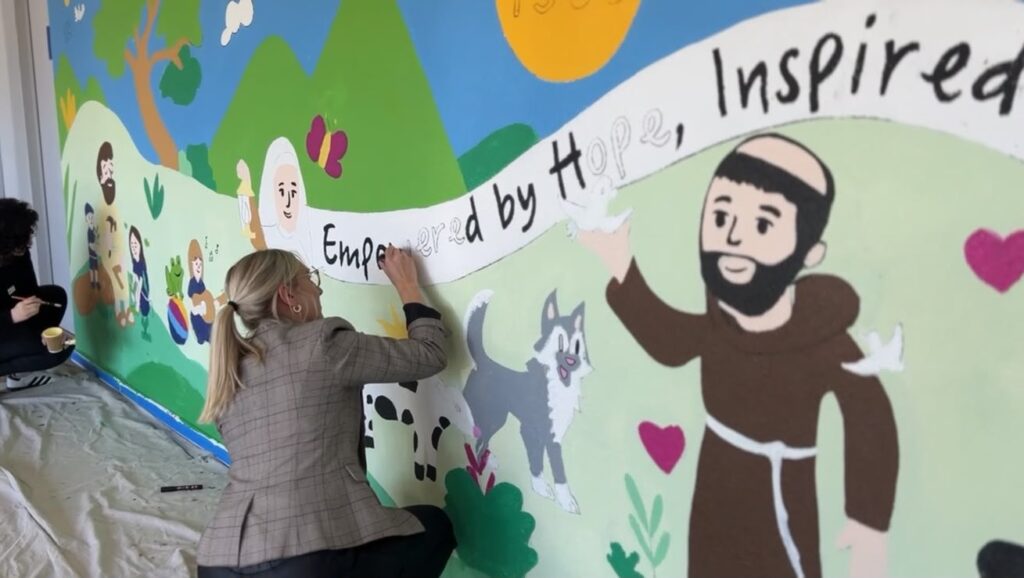 A teacher painting the lettering on the St Francis of Assisi School mural