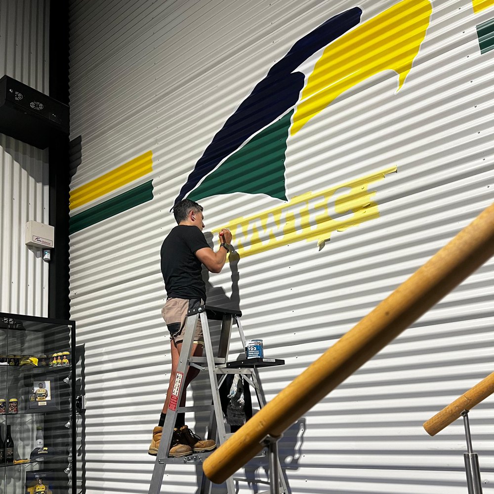 Diegodalo hand-painting the WWTFC logo on corrugated metal at height for Craig Arthur Transport